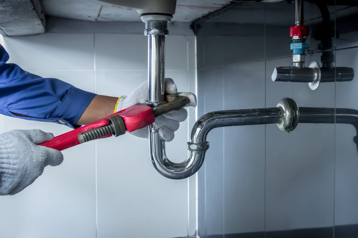 Plumber hands holding wrench repairing sink pipe